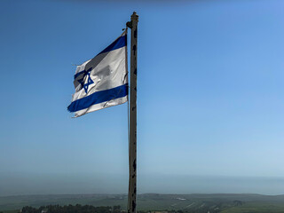 Partially torn israeli flag is waving in the wind on blue sky background