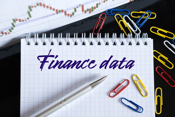 On the desktop are a forex chart, paper clips, a pen and a notebook in which it is written - Finance data