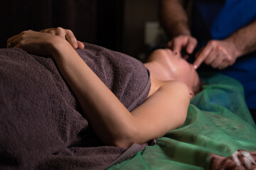 Professional facial massage. Male masseur makes procedures on a female face on a dark background.