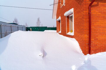 Red brick farmhouse with huge snowdrifts near the windows after snowfall in winter