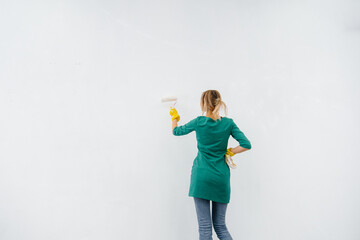 A young girl paints a white wall with a roller. Repair of the interior.