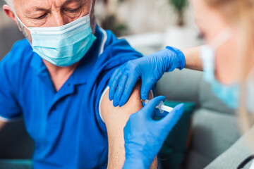 Female doctor vaccinating senior male patient at home. Coronavirus, Covid-19 concept.