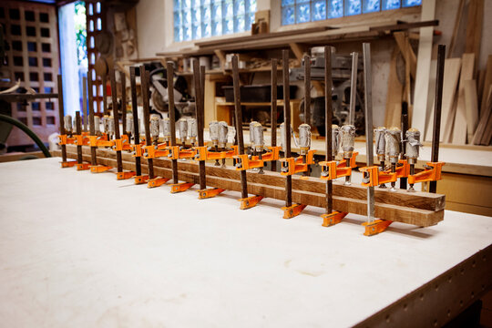 Row bar clamps holding wooden planks on table at workshop