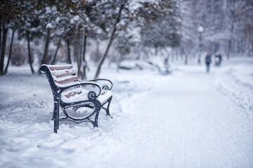 lonely park bench during snowfall on winter day