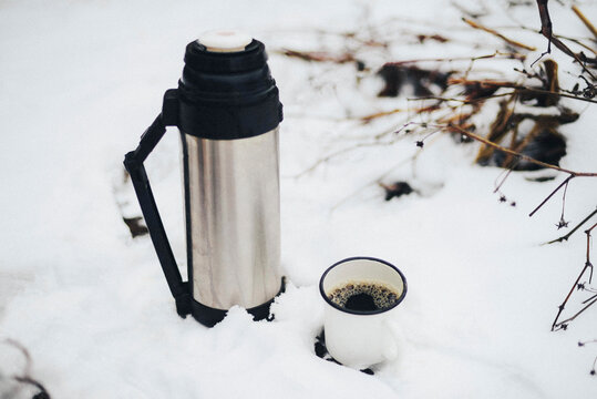 Close-up of insulated drink container by mug with black coffee on snow