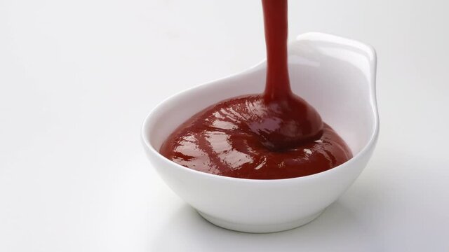 Pouring ketchup in bowl on white background