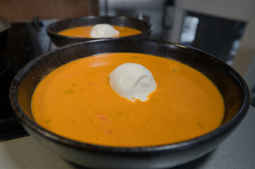 Zwei schwarze Teller mit Paprika Kokossuppe mit Garnelen  und Burrata