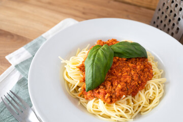 Plate of spaghetti with vegan bolognese sauce made with textured peas and decorated with some green basil leaves