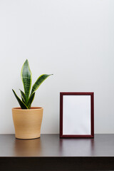 Brown wooden frame mockup in portrait orientation with a cactus in a pot on dark workspace table and white background