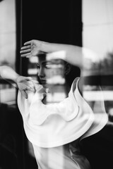 Fototapeta na wymiar Black white photo portrait of beautiful woman in white dress posing near window