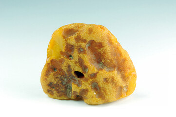 Loose natural genuine unpolished baltic butterscotch egg yolk opaque royal yellow color amber raw rough stone piece. Sky blue and white gradient background. Sharp details macro.