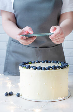 Professional food blogger taking pictures on smartphone. White cake with cream cheese and fresh blueberries.