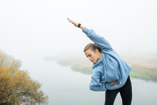 Young fit sportswoman in blue hoodie and black leggins doing side bends