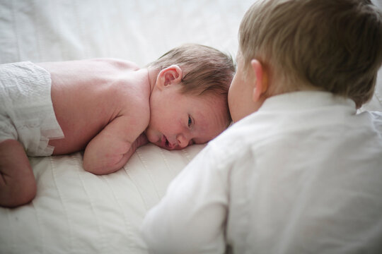 High angle view of brother kissing newborn lying on bed at home