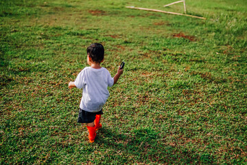 a happy kid walking on the grass wearing a red rubber boot carrying a magnifying glass