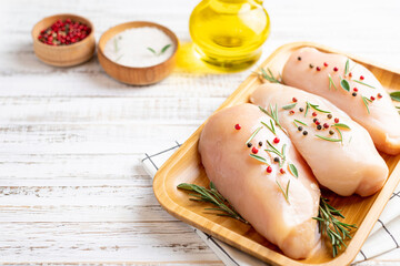 Chicken fillet with herbs and spices on white wooden table close up. Chicken meat with ingredients for cooking. Copy space.
