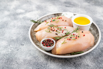 Raw uncooked chicken breasts on grey concrete background, chicken meat with ingredients for cooking. Copy space