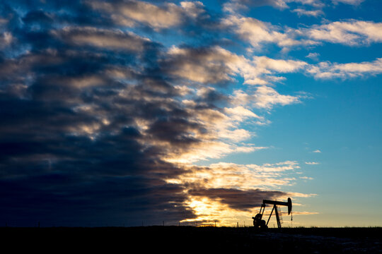 Mid distance view of silhouette pumpjack at oil industry on field against cloudy sky during sunset