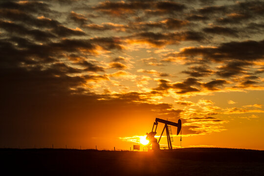 Mid distance view of silhouette pumpjack at oil industry against cloudy sky during sunset