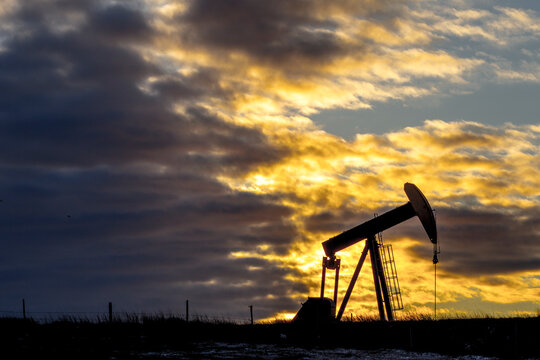 Pumpjack at oil industry against cloudy sky during sunset
