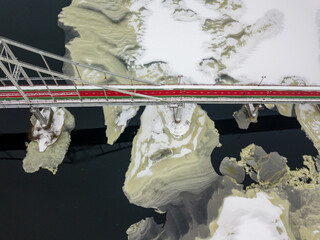 Red-green pedestrian bridge over the Dnieper river in Kiev. Snow patterns on the river. Aerial drone view. Winter snowy morning.