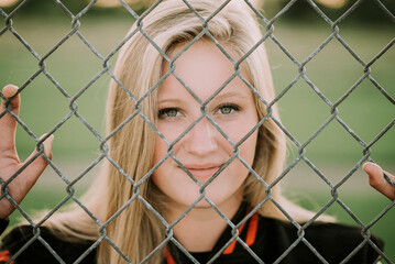 Portrait of softball player standing by fence at playing field