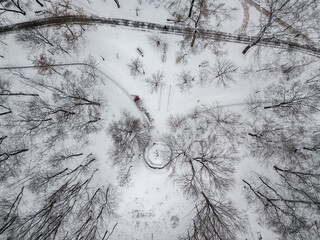 Red tractor removes snow in the park. Aerial drone view. Winter snowy morning.