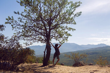 woman in a hat stands by a tree on a mountain in the summer in the Crimea