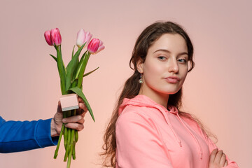 Young woman in a pink hoodie is presented with a bouquet of tulips and a pink box. Has no idea what to do.