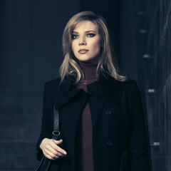 Young fashion blonde woman in black coat with leather handbag