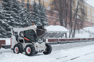 A small loader excavator bobcat removes snow from the sidewalk near the Kremlin walls during a...