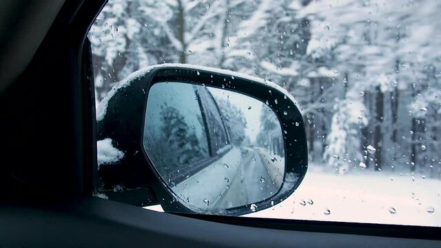 Car driving on snow covered road through winter snowy forest. View from side mirror.