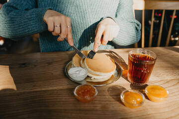 The girl cuts delicious pancakes with a knife. Nearby is a glass of tea and various fruit jams.