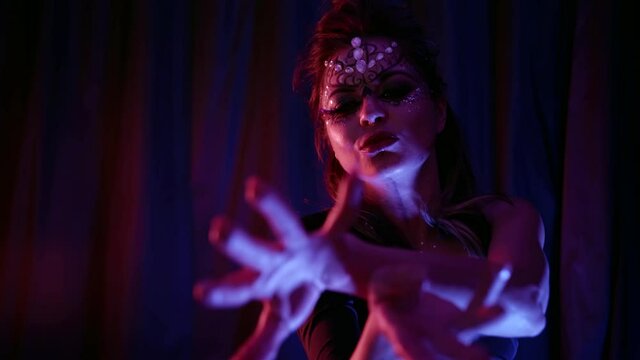 A beautiful passionate woman dances, makes swings of her head and hair while in the room against the background of blue curtains. She has a beautiful makeup with rhinestones.