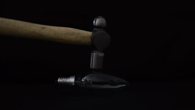 Un martillo golpeando una bombilla y rompiéndola en pedazos sobre fondo negro