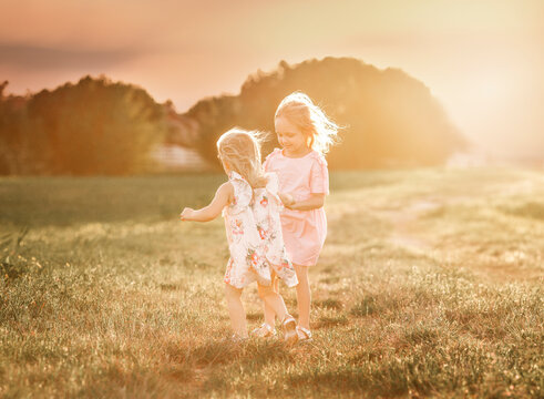 Sisters walking on grassy field against sky during sunset