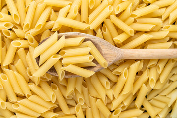 A wooden spoon over a Lot of penne macaroni background texture