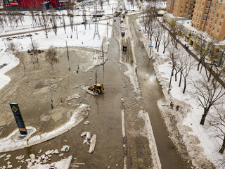 The tractor clears the water on the road. Aerial drone view. Winter snowy morning.