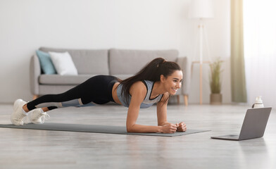 Sporty millennial woman planking in front of laptop