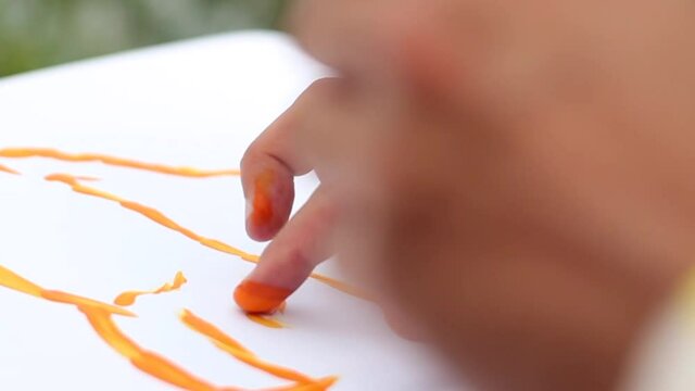 Woman's hand draws a drawing on white paper with a yellow paint finger