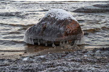 A countryside snowy frozen stone with sunset through the horizon surrounded by pine trees under the blue sky
