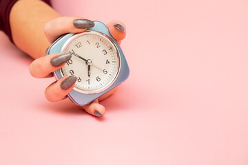 female hand holds alarm clock on pink background