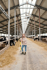 Young female worker of large contemporary animal farm standing in aisle