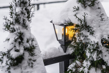 Illuminated lantern on snow and white cedar.