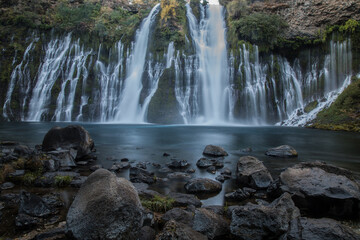 Fototapeta na wymiar Burney Falls in early dawn light with stones in the foreground.