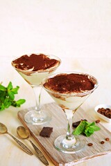Tiramisu, dessert with biscuit cookies and mascarpone cream in triangular glasses on a light concrete background. Dessert recipes without baking. Desserts in glasses.