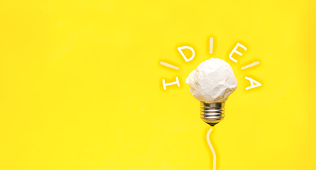 Composition with crumpled paper light bulb,  and word IDEA on on a yellow background. Space for text
