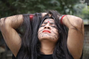 A southeast Asian brown woman protesting gender based violence by writing anti violence against women and girls messages all over her face and looking angry and sad