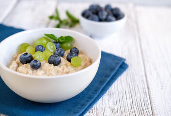 Porridge with blueberry and grapes on napkin and wooden background. Fresh and healthy breakfast