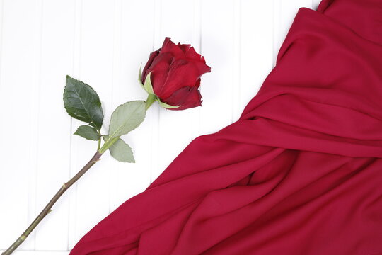 Czerwona róża i czerwona tkanina na białym blacie